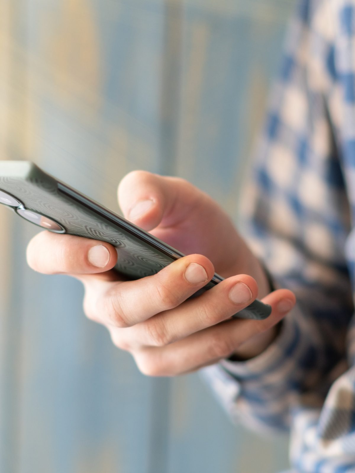 Close-up image of male hands using smartphone at night on city shopping street, searching or social networks concept